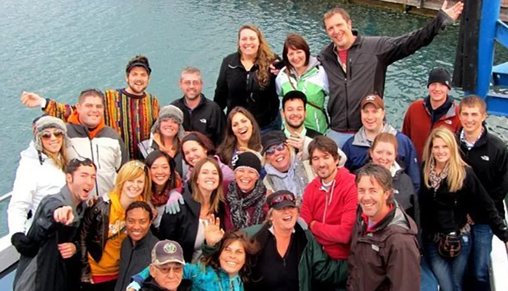 A group of smiling people pose for a photo possibly on a boat or dock exhibiting a cheerful and casual atmosphere