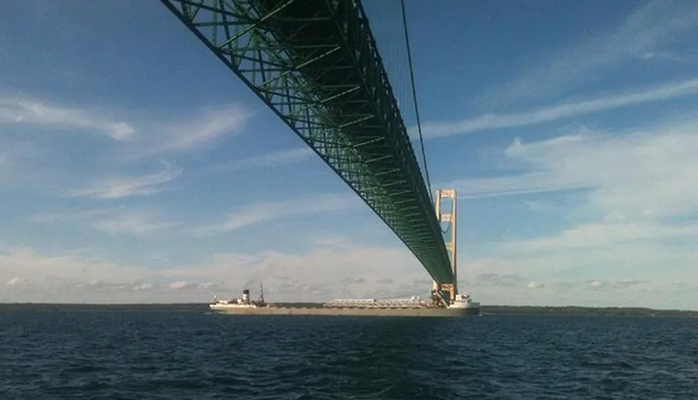 A large freighter is passing under a towering suspension bridge over a body of water viewed from a boat or shoreline