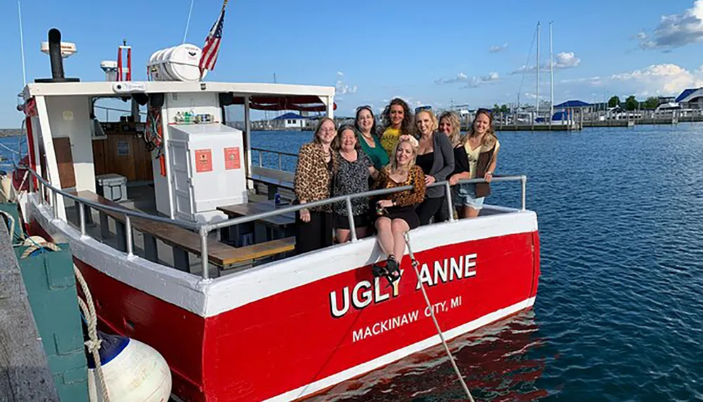 A group of women is posing for a photo on the stern of the Ugly Anne boat docked in Mackinaw City MI on a sunny day with clear skies and calm waters