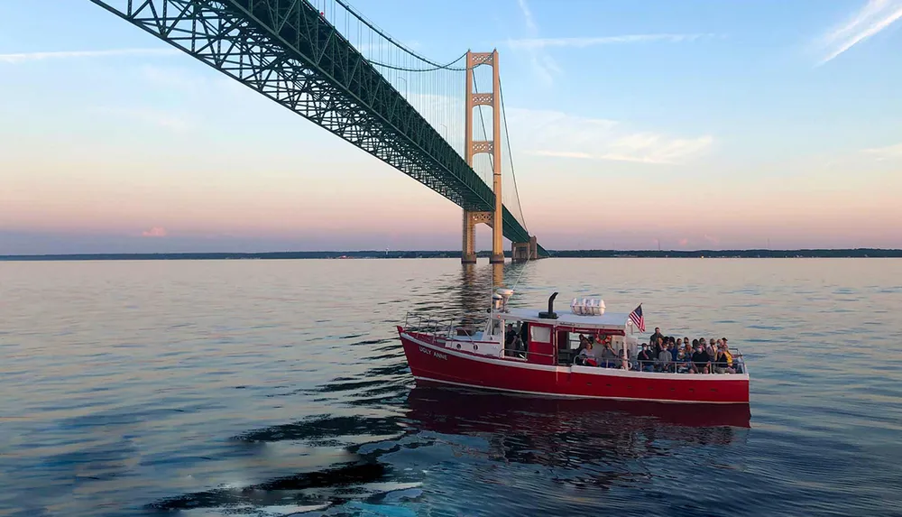 A tour boat named Ugly Anne is cruising near a large suspension bridge during a calm evening