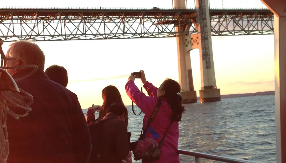 Passengers are capturing the sunset views from a boat near a large bridge