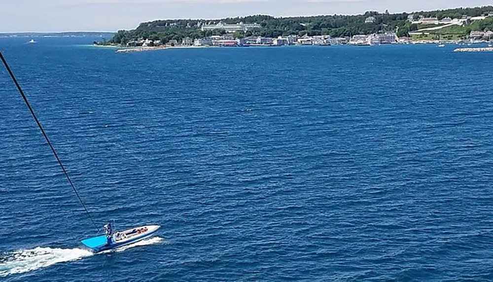 A speedboat is cruising on the blue waters near a coastline dotted with buildings under a clear sky