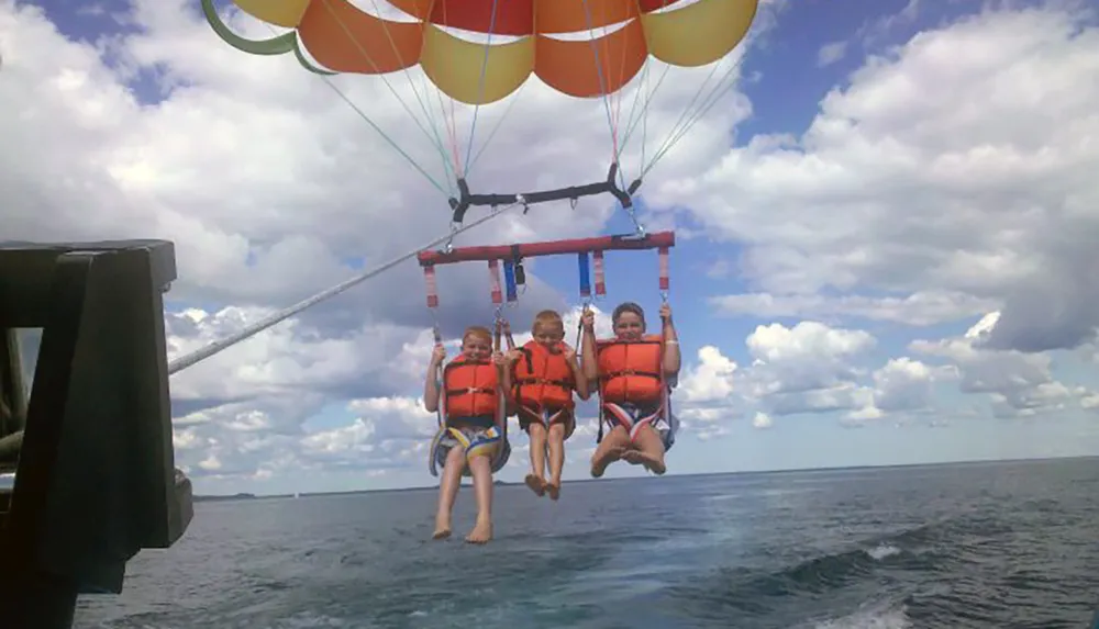 Three people are parasailing over the sea enjoying an adventurous time in the sky under a colorful parachute