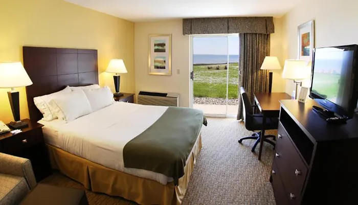 A neatly arranged hotel room with a king-size bed two lamps a desk area and a sliding glass door offering a view of the ocean