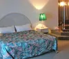 The image shows a neatly made bed with a green bedspread flanked by a nightstand and lamp in a room with a simple decor