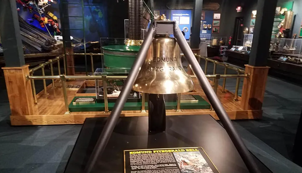 The image shows a brass ships bell displayed on a stand with an informational plaque in what appears to be a museum setting