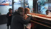 Visitors are engaged in examining a ship model and reading information on display at a maritime museum exhibit.