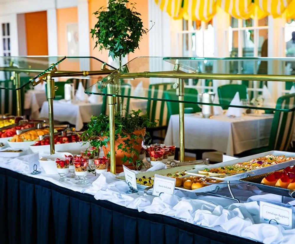 A buffet table with a variety of dishes and decorative plants is set up in an elegant dining room with green and yellow accents
