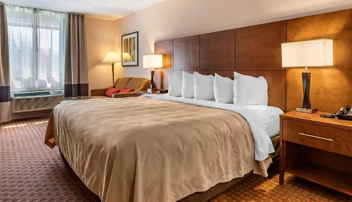 This is a neatly arranged hotel room with a large bed a seating area and warm lighting