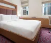 The image shows a neatly arranged hotel room with a large bed modern furnishings and a city view from the window