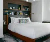 The image depicts a modern and neatly organized bedroom with a large bed stylish headboard built-in shelves displaying various decorative items and a subtle color palette complemented by patterned accents