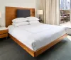 This image shows a neatly made bed with white bedding in a bright modern bedroom with a balcony door open to the outside