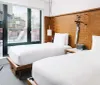 The image shows a modern hotel room with two twin beds wooden accents and a sliding glass door leading to a balcony