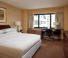 This image shows a tidy hotel room with a large bed a window with a city view a desk area and tasteful decorations creating a comfortable and inviting space