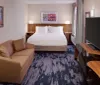 The image shows a neatly arranged hotel room with a large bed a sofa a work desk with a flat-screen television and decorative artwork on the walls
