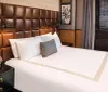 The image depicts a neatly made bed with white linens in a stylishly furnished room featuring an elegantly tufted leather headboard and tasteful decor