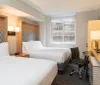 The image shows a modern and neatly arranged hotel room with two beds a desk area mounted television and a window