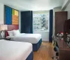 A modern hotel room featuring a large bed with a colorful headboard a working desk a seating area and a window with a view of an adjacent building
