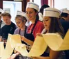 A group of individuals wearing white chef hats appear engaged and happy as they participate in a cooking class or culinary workshop