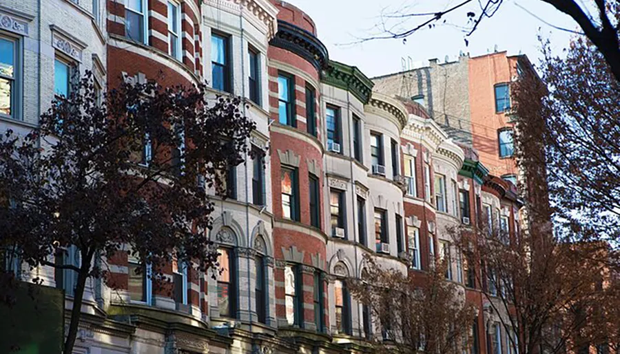 This image shows a row of ornate, multistory residential buildings with bay windows and a mix of red brick and stone facades, typical of certain historic urban neighborhoods.