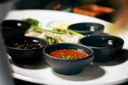 A white plate hosts several small black bowls with various sauces and some garnishes.