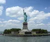 The image shows the Statue of Liberty standing on Liberty Island against a backdrop of blue skies and scattered clouds