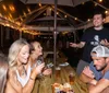 A group of people is enjoying an evening at an outdoor patio socializing and laughing under string lights