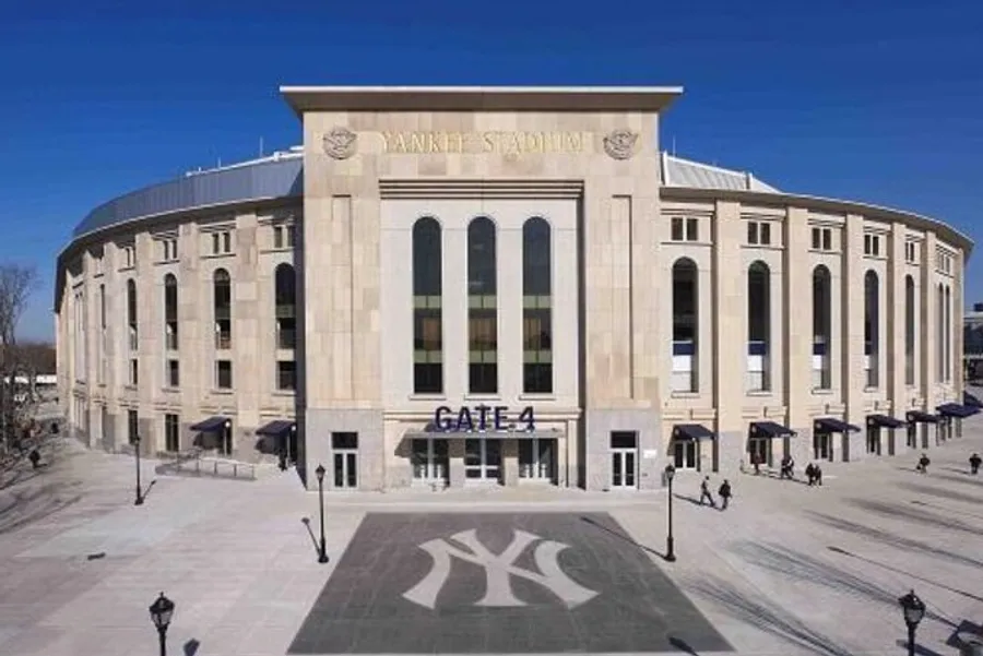 The image displays the exterior of Yankee Stadium with Gate 4 visible and a few people walking nearby.