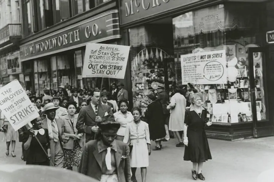 A group of people is marching in front of an F. W. Woolworth Co. store, carrying signs indicating a strike and a call for support from the public to not patronize the store.