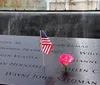 An American flag and a rose are placed on the engraved names at a somber memorial site signifying remembrance and honor
