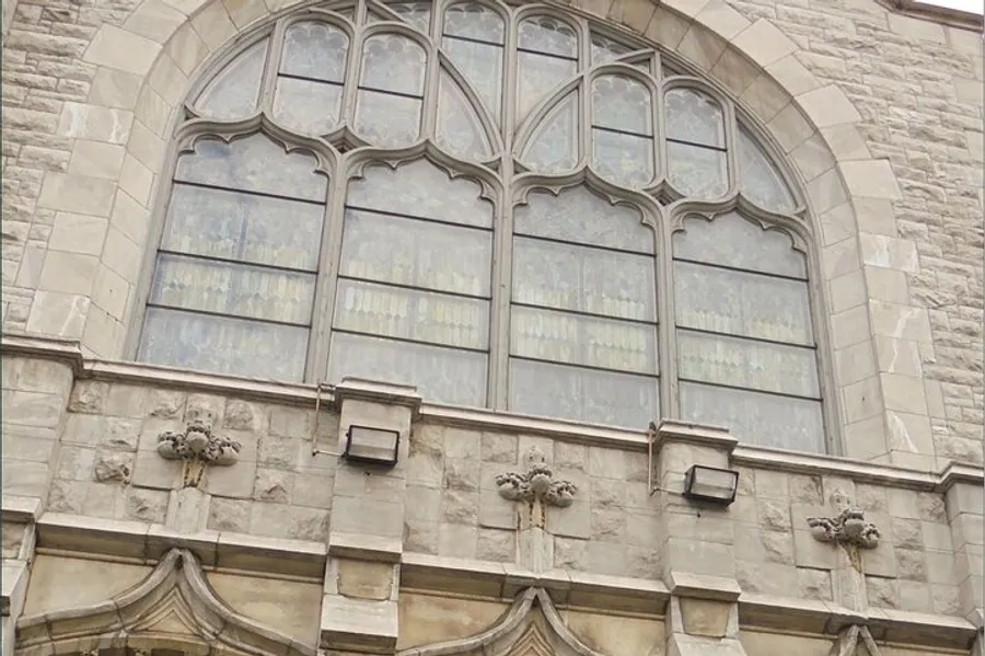 The image shows a large ornate gothic-style window with stained glass, set in a stone building with decorative stonework detailing.