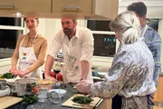 A group of people is actively engaged in a cooking class or workshop, preparing various ingredients on a kitchen counter.