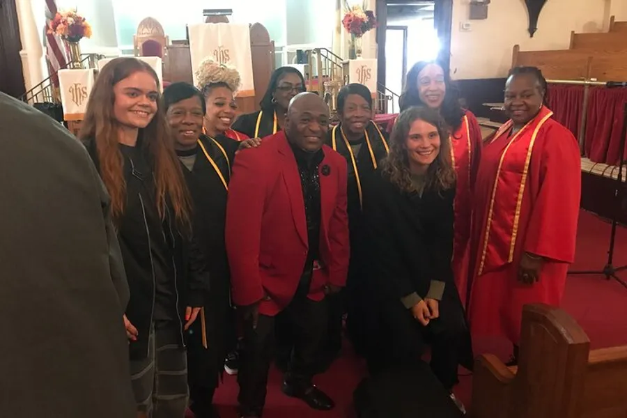 A group of smiling people, some in red and gold choir robes, are posing for a photo inside a church.
