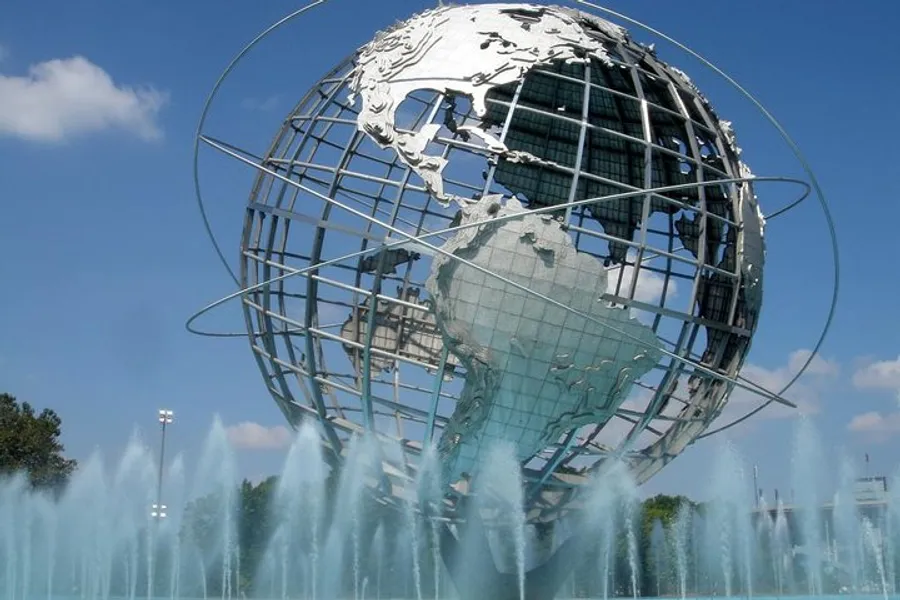 The image shows the Unisphere, a spherical stainless steel representation of the Earth, surrounded by fountain sprays and located at Flushing Meadows–Corona Park in Queens, New York.