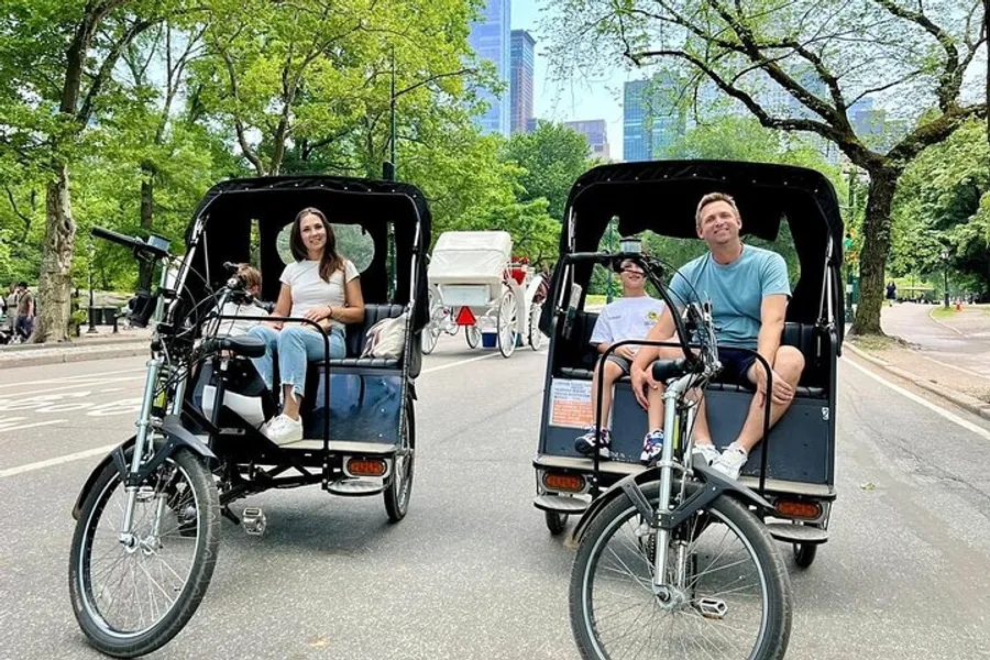Two people are enjoying a ride in pedicabs through a park with tall buildings in the background.