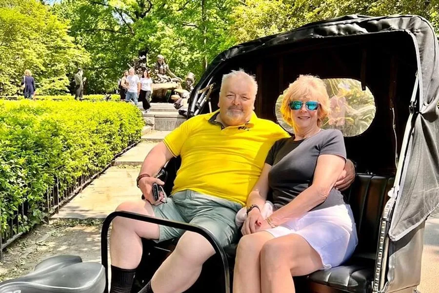 A smiling couple is seated comfortably in a pedicab, enjoying a sunny day in a park with green foliage and a statue in the background.