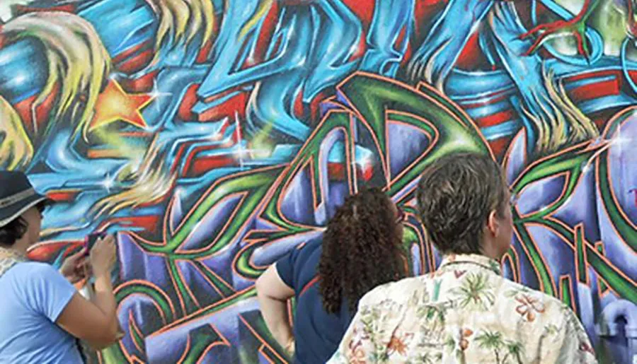 Three people are observing a colorful, abstract graffiti wall mural.