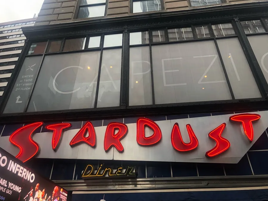 The image shows the exterior of a building with a neon sign that reads STARDUST in bright red, with a partially visible sign reading Diner beneath it.