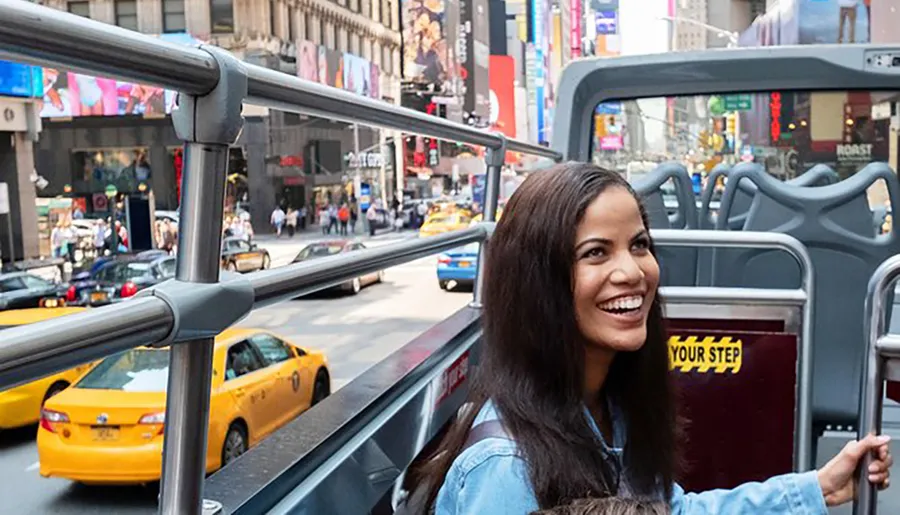 A smiling woman is enjoying a sightseeing bus tour in a bustling cityscape filled with yellow taxis and vibrant billboards.