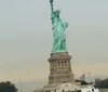 The image shows the iconic Statue of Liberty with a Statue Cruises ferry passing by in the foreground