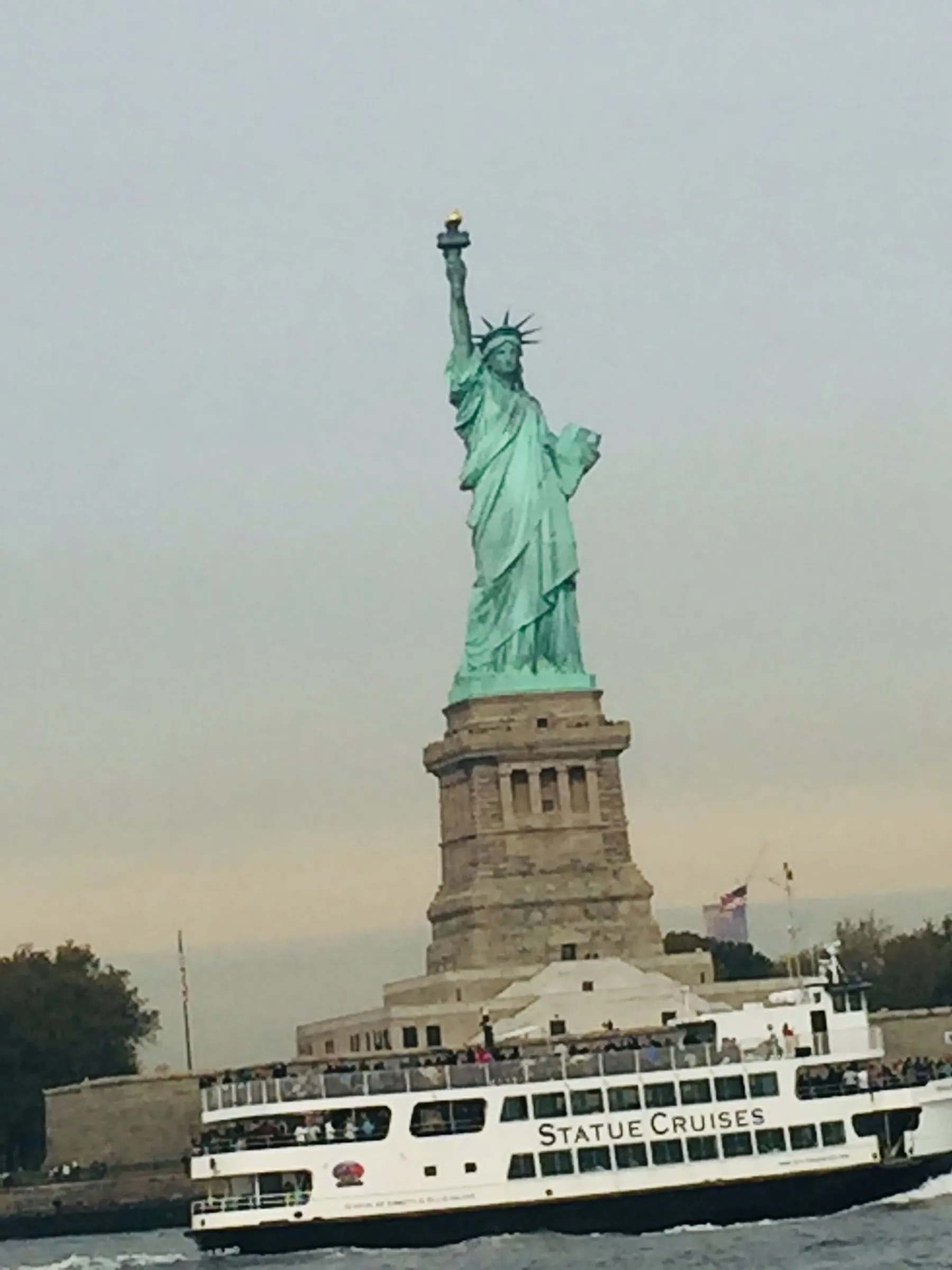 The image shows the iconic Statue of Liberty with a 'Statue Cruises' ferry passing by in the foreground.