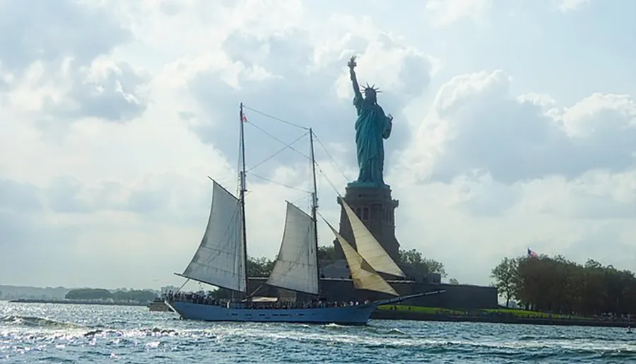 A schooner sails by the Statue of Liberty on a cloudy day.