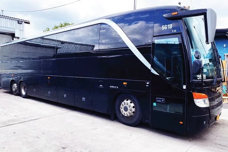 A sleek black tour bus with a modern design is parked at a facility with an overcast sky in the background.
