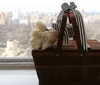 A wooden basket with white roses and a striped ribbon sits on a windowsill with a blurred cityscape in the background