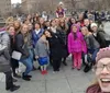 A group of smiling people of various ages are posing for a selfie with one person in the foreground holding the camera and extending her arm to capture everyone
