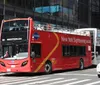 A red double-decker sightseeing tour bus is navigating through a busy urban street