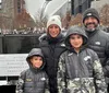 A family of four dressed in winter clothing is smiling for the photo in front of the 911 Memorial reflecting pools in New York City