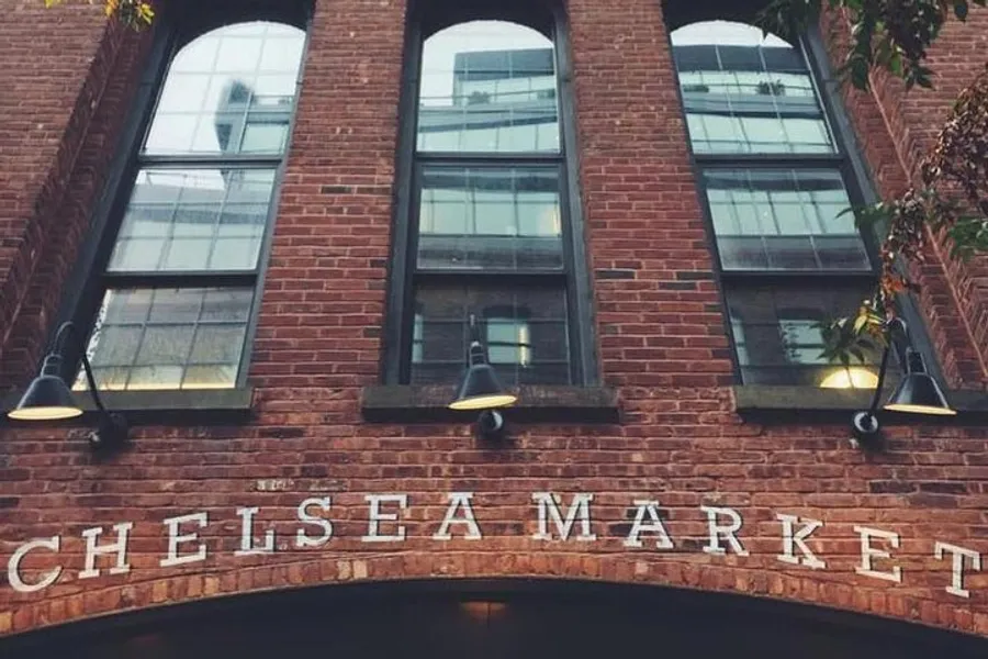 The image displays the exterior of the Chelsea Market with its name in large letters on a brick facade, flanked by overhead lights.
