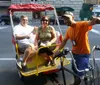 A family is enjoying a ride on an urban pedicab with the driver at the front and a woman holding a red parasol seated behind him