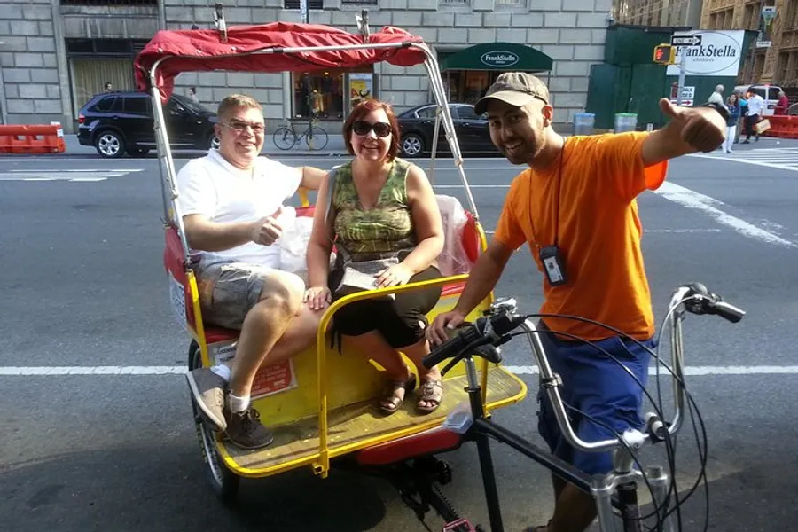 A rickshaw driver gives a thumbs-up while two passengers smile at the camera in the back seat of a pedicab on a sunny city street.
